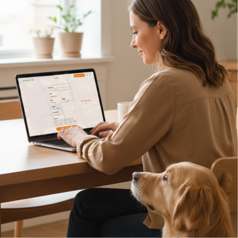 Woman using a laptop at a desk with a dog sitting next to her